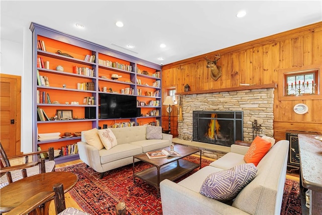 living room with wood walls, a stone fireplace, and built in features