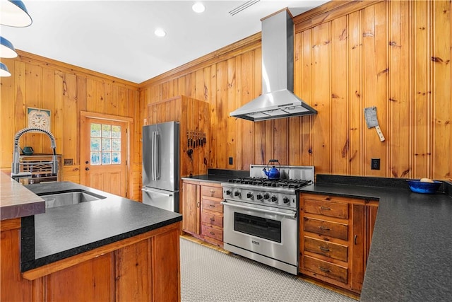 kitchen featuring sink, wall chimney exhaust hood, wooden walls, appliances with stainless steel finishes, and ornamental molding