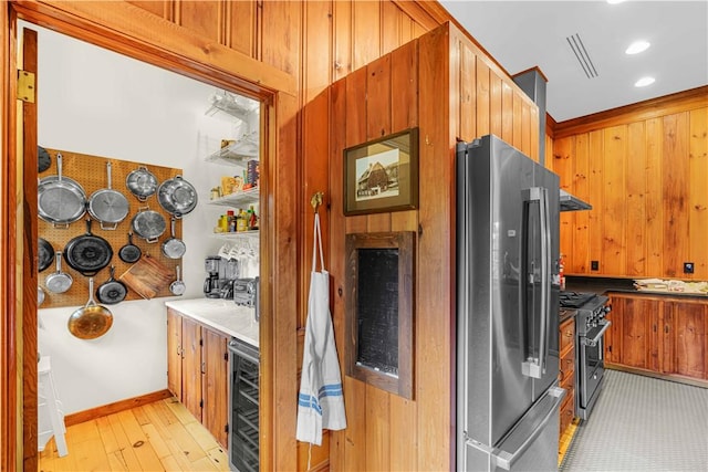 kitchen featuring wooden walls, beverage cooler, stainless steel appliances, and light wood-type flooring