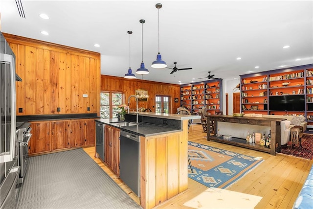 kitchen featuring light wood-type flooring, stainless steel appliances, wooden walls, sink, and pendant lighting