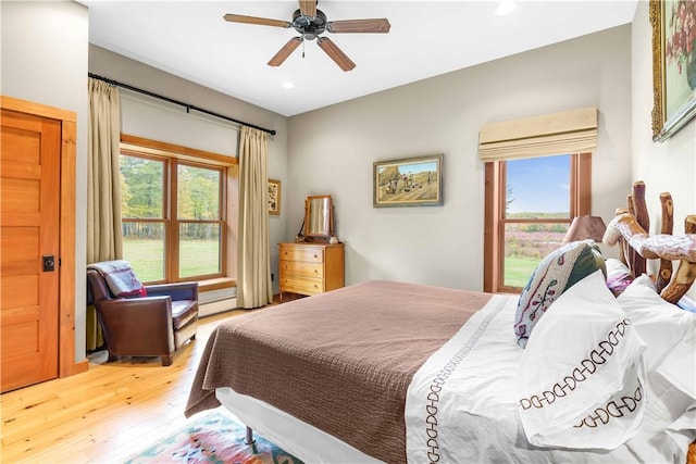 bedroom featuring hardwood / wood-style flooring, multiple windows, a baseboard heating unit, and ceiling fan