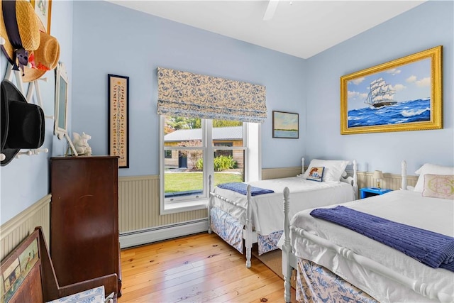 bedroom with hardwood / wood-style floors, ceiling fan, and a baseboard heating unit