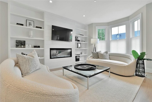 living room featuring built in features, recessed lighting, a large fireplace, and wood finished floors