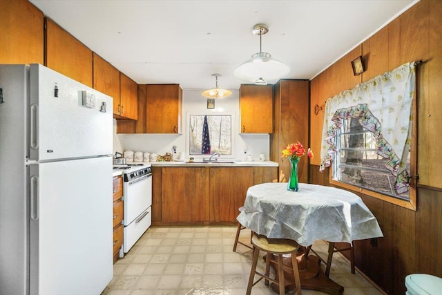 kitchen featuring white appliances, decorative light fixtures, wooden walls, and sink