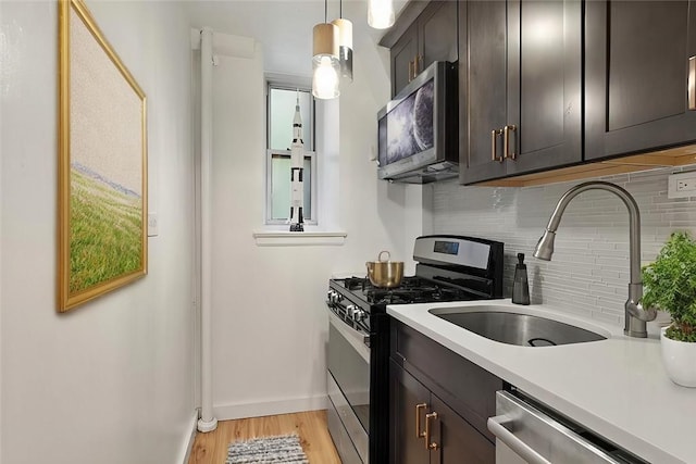 kitchen featuring hanging light fixtures, light hardwood / wood-style flooring, backsplash, dark brown cabinets, and appliances with stainless steel finishes