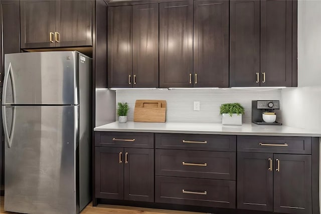 kitchen with light wood-type flooring, dark brown cabinets, backsplash, and stainless steel refrigerator