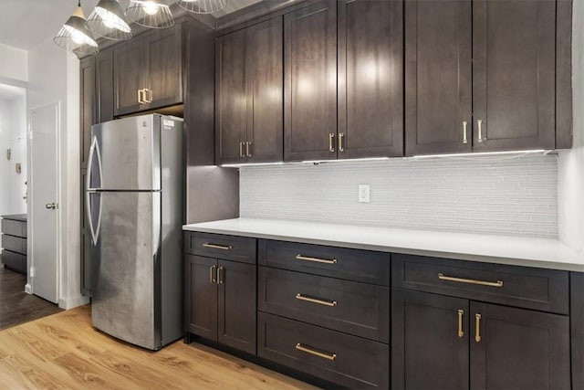 kitchen featuring stainless steel refrigerator, hanging light fixtures, light hardwood / wood-style floors, decorative backsplash, and dark brown cabinets