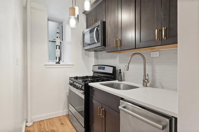 kitchen with appliances with stainless steel finishes, tasteful backsplash, dark brown cabinets, decorative light fixtures, and light hardwood / wood-style flooring