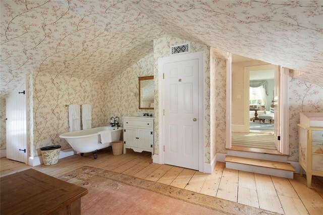 bathroom with hardwood / wood-style floors, vanity, a bathing tub, and lofted ceiling