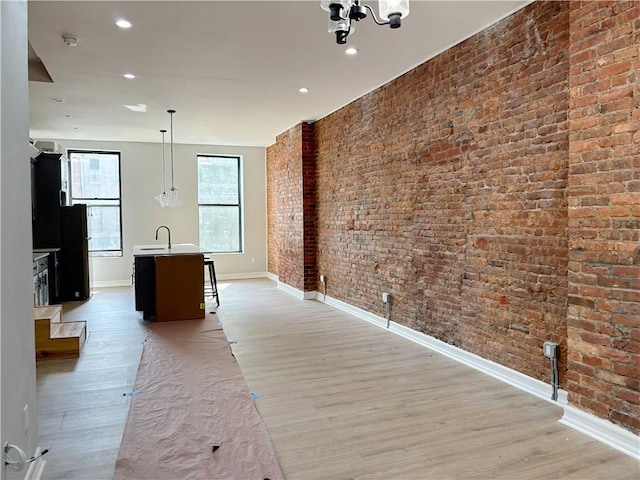 kitchen with brick wall, sink, pendant lighting, light hardwood / wood-style flooring, and an island with sink