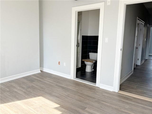 unfurnished bedroom featuring ensuite bathroom, wood-type flooring, and tile walls