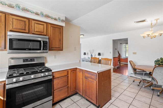 kitchen with kitchen peninsula, appliances with stainless steel finishes, light tile patterned floors, and a notable chandelier