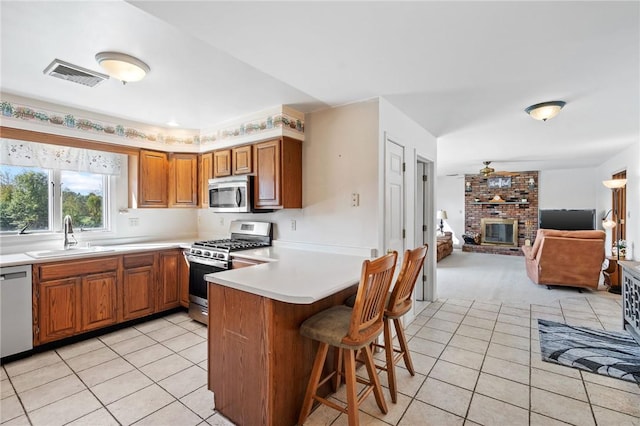 kitchen with a kitchen bar, appliances with stainless steel finishes, kitchen peninsula, sink, and a fireplace