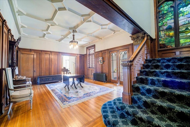 interior space with radiator, coffered ceiling, light hardwood / wood-style flooring, a chandelier, and wood walls