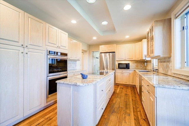 kitchen featuring a center island, black appliances, light hardwood / wood-style flooring, tasteful backsplash, and light stone counters