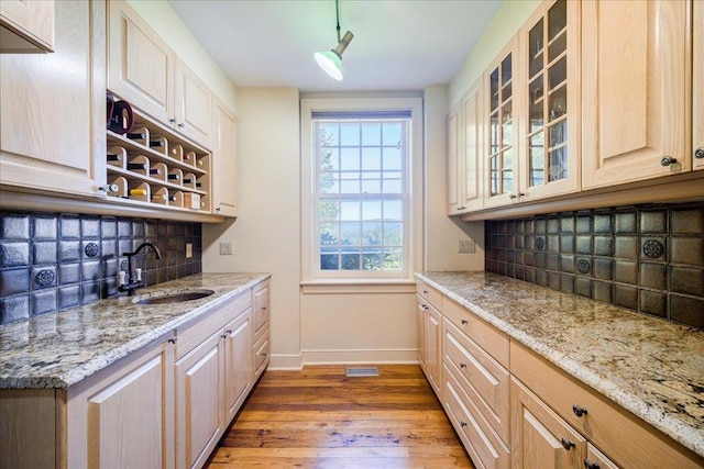 kitchen featuring light stone countertops, sink, backsplash, light brown cabinetry, and hardwood / wood-style flooring