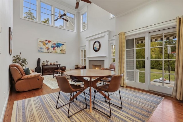 dining space with ceiling fan, crown molding, wood-type flooring, and a high ceiling