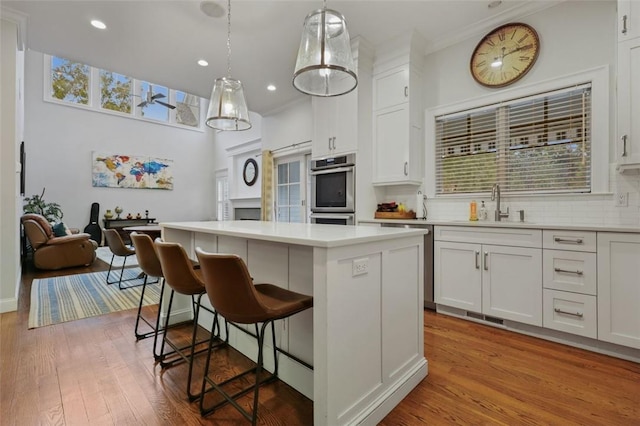 kitchen featuring double oven, sink, decorative light fixtures, white cabinets, and a center island