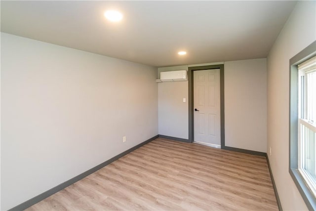 empty room with a wall unit AC, a wealth of natural light, and light hardwood / wood-style floors