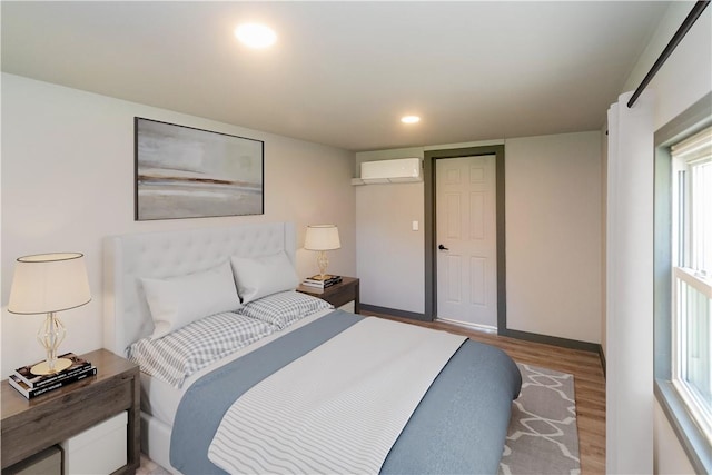 bedroom featuring hardwood / wood-style flooring, a wall unit AC, and multiple windows