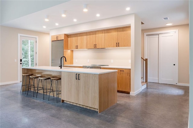 kitchen featuring light brown cabinets, a center island with sink, sink, stainless steel fridge, and a breakfast bar area