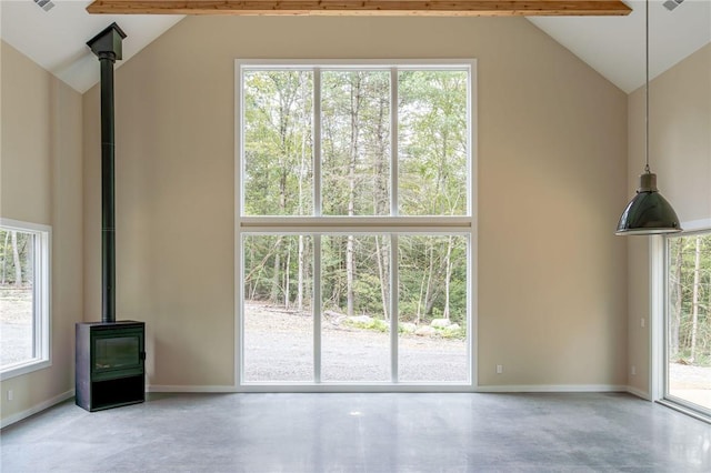 unfurnished living room featuring beam ceiling, a wood stove, and a wealth of natural light