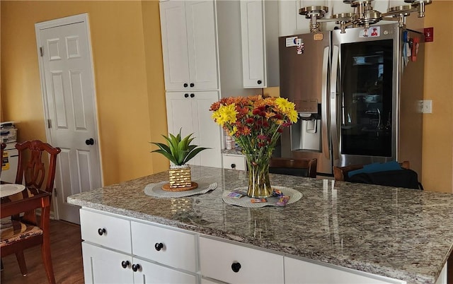 kitchen with white cabinetry, a center island, light stone countertops, dark hardwood / wood-style flooring, and stainless steel fridge