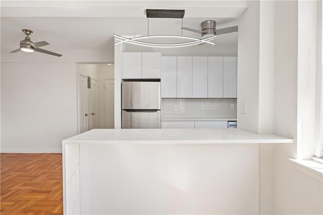 kitchen with light parquet floors, white cabinets, ceiling fan, kitchen peninsula, and stainless steel refrigerator