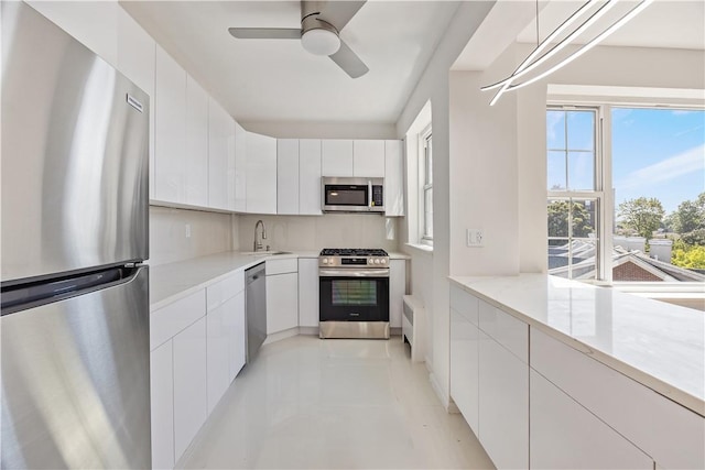 kitchen featuring sink, ceiling fan, appliances with stainless steel finishes, white cabinetry, and radiator heating unit