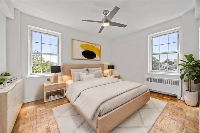 bedroom with ceiling fan, radiator heating unit, and light parquet floors