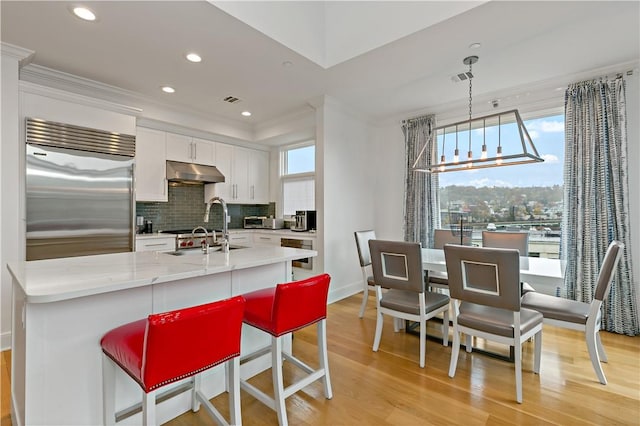 kitchen with a healthy amount of sunlight, light hardwood / wood-style flooring, white cabinets, built in refrigerator, and hanging light fixtures