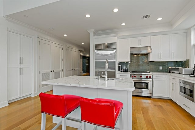 kitchen featuring premium appliances, white cabinetry, light hardwood / wood-style flooring, and an island with sink