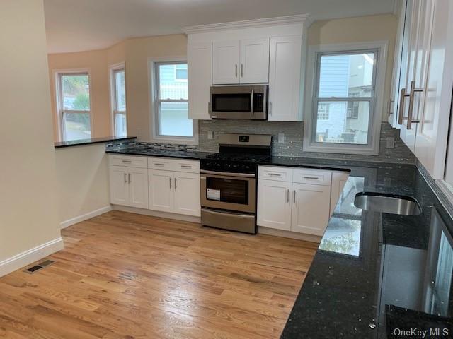 kitchen featuring tasteful backsplash, white cabinets, dark stone counters, and appliances with stainless steel finishes