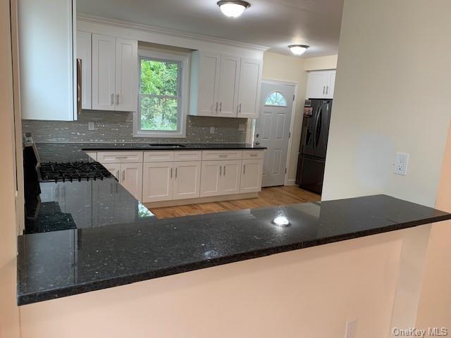 kitchen featuring black refrigerator, dark stone countertops, white cabinetry, and kitchen peninsula