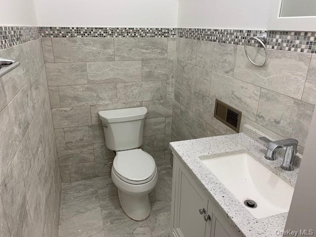 bathroom featuring vanity, tile walls, and toilet