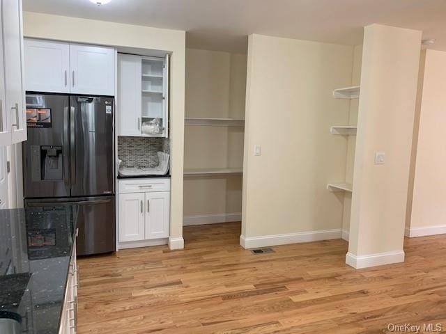 kitchen with tasteful backsplash, dark stone counters, refrigerator with ice dispenser, light hardwood / wood-style flooring, and white cabinets