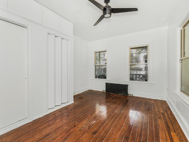 unfurnished bedroom featuring ceiling fan, radiator heating unit, dark wood-type flooring, and a closet