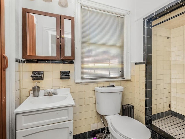 bathroom featuring vanity, toilet, a tile shower, and tile walls