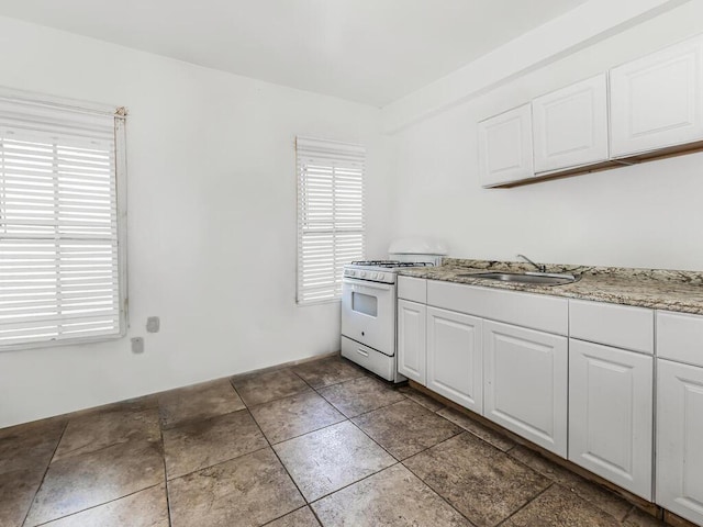 kitchen featuring white cabinets, white gas range oven, light stone countertops, and sink