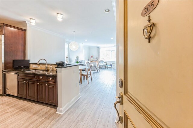 kitchen with light wood-type flooring, tasteful backsplash, sink, pendant lighting, and dark stone countertops