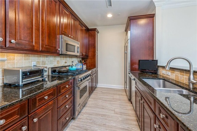 kitchen featuring backsplash, dark stone counters, sink, light wood-type flooring, and stainless steel appliances