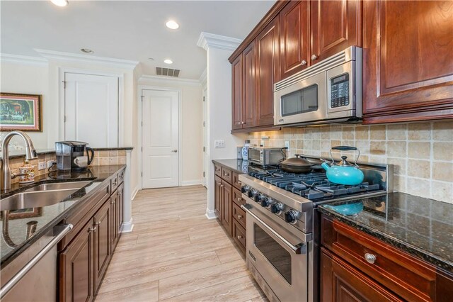 kitchen with sink, backsplash, dark stone countertops, light hardwood / wood-style floors, and appliances with stainless steel finishes