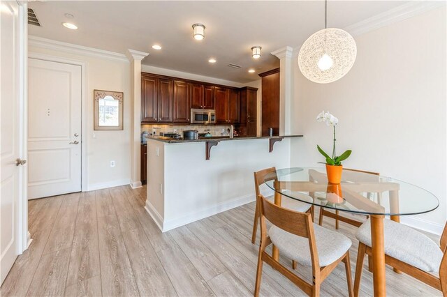 kitchen featuring backsplash, kitchen peninsula, decorative light fixtures, a breakfast bar area, and light wood-type flooring