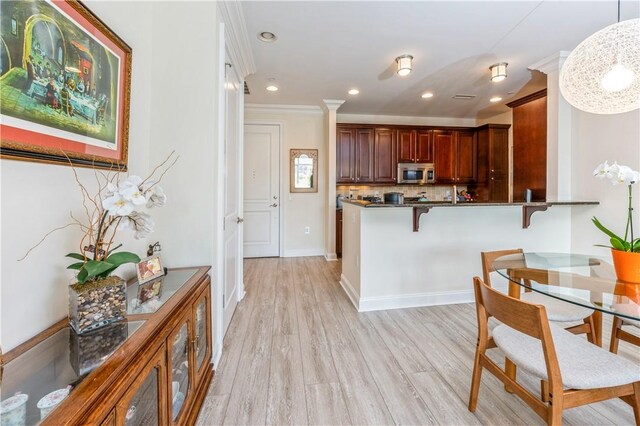 kitchen featuring backsplash, kitchen peninsula, pendant lighting, light hardwood / wood-style floors, and a kitchen bar