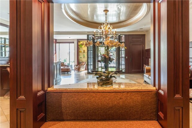 interior space with light stone countertops, a raised ceiling, pendant lighting, a notable chandelier, and light tile patterned flooring