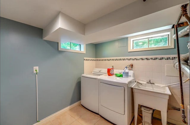 laundry room with washing machine and clothes dryer, light tile patterned floors, a wealth of natural light, and tile walls