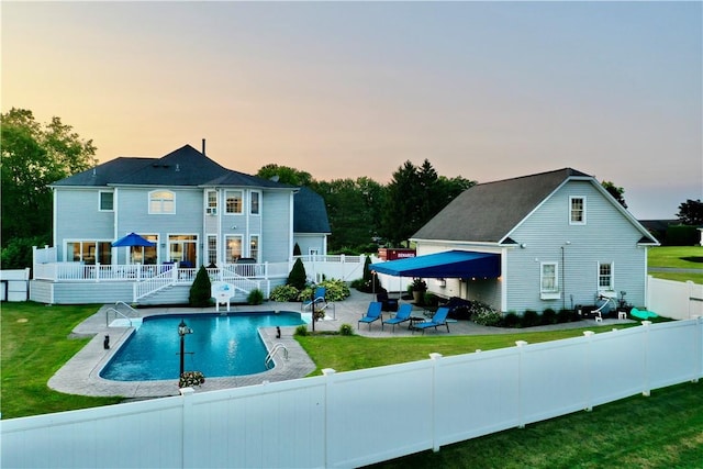 back house at dusk featuring a lawn, a fenced in pool, and a patio