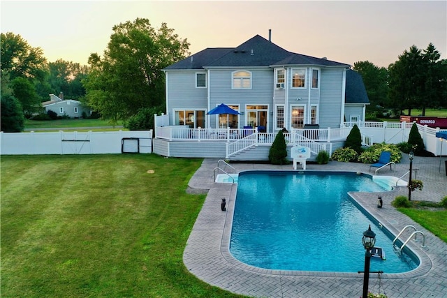 back house at dusk with a pool side deck and a lawn