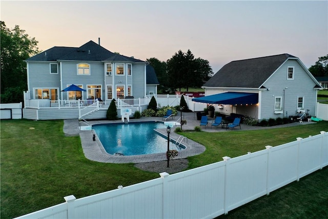 pool at dusk featuring a lawn, a patio area, and a deck