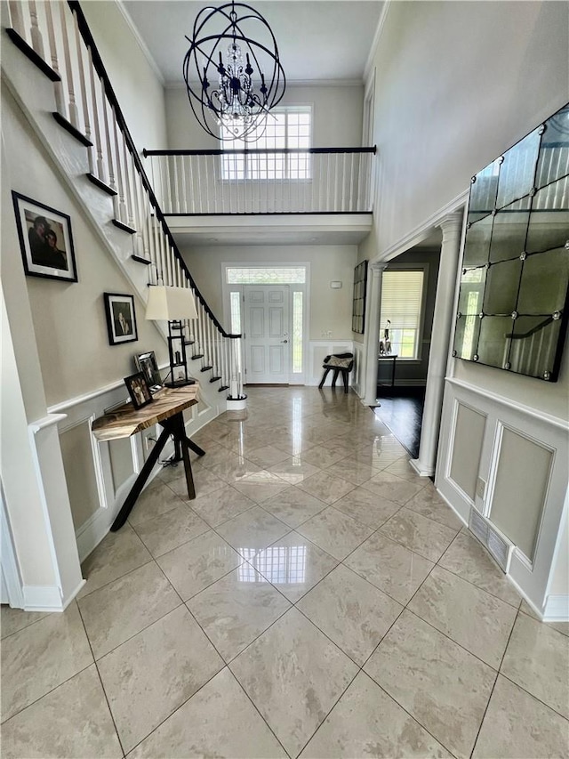 foyer entrance with a notable chandelier, a healthy amount of sunlight, crown molding, and a high ceiling